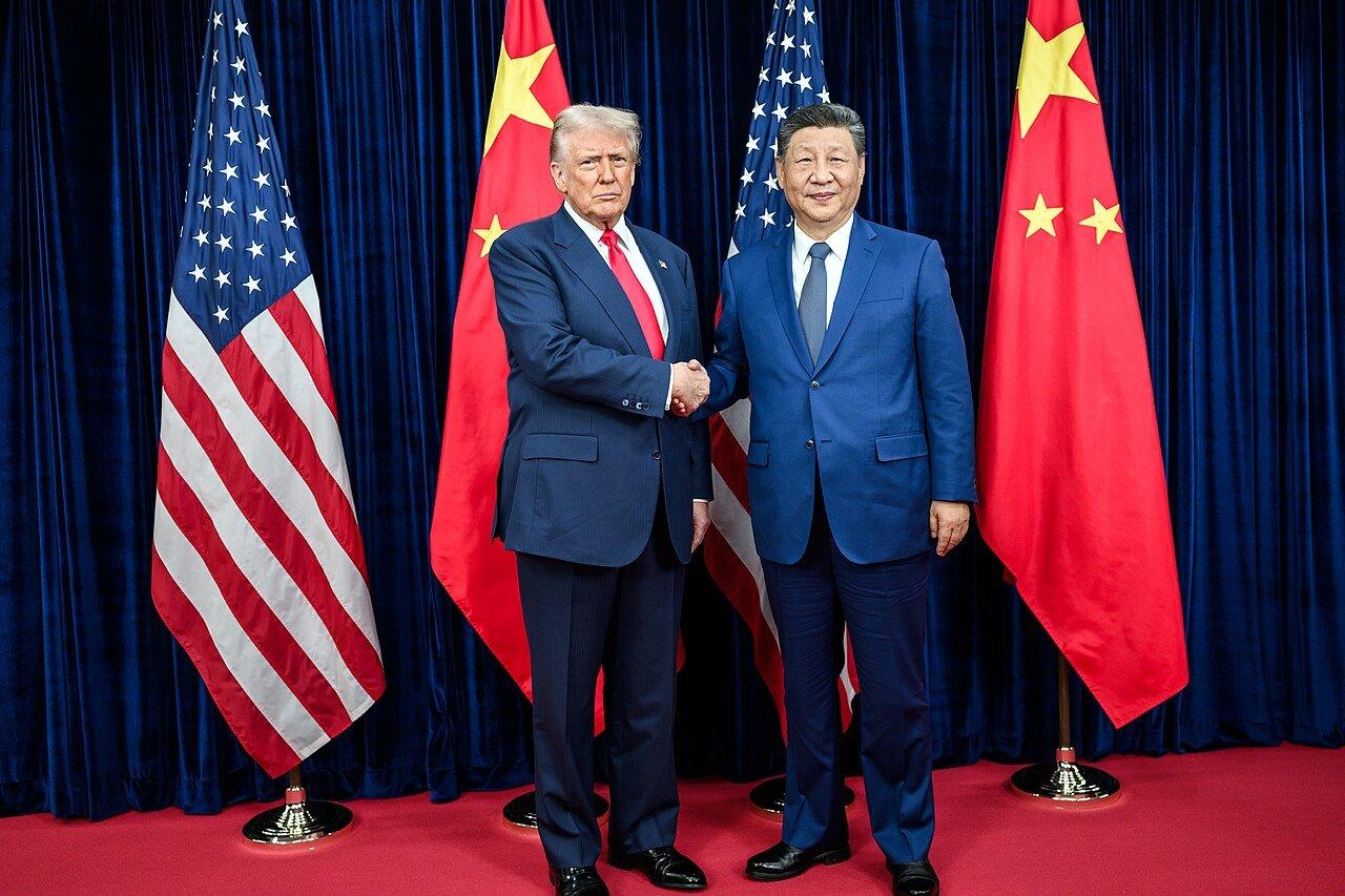 Donald Trump greets Xi Jinping before their bilateral meeting at Gimhae International Airport in Busan, South Korea, in October 2025 — the summit that produced the truce now extended.
